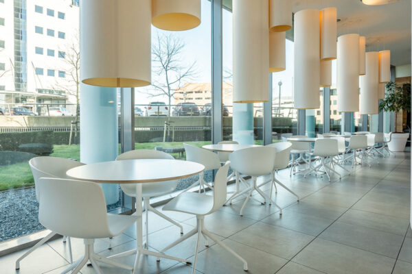 Moderne, lichte kantine met witte tafels en stoelen bij Rivium Quadrant, met uitzicht op een kantooromgeving.